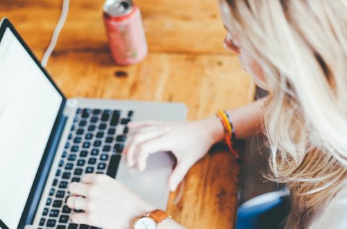 Kobieta pracująca przy laptopie w kawiarni, trzymając kawę